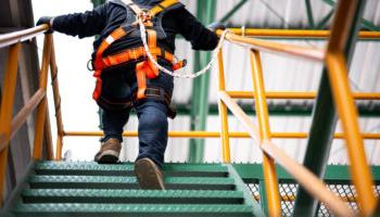 A Construction Worker Climbing Stairs While Wearing A Safety Harness Locked To The Nearby Railing.